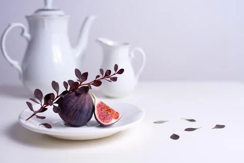 Two figs on a white plate with a branch of barberry, white tea pot and cup on Stock Photos