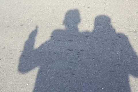 Two figures stand close, casting shadows on asphalt Stock Photos