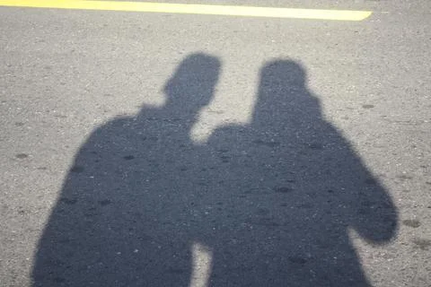 Two figures stand close, casting shadows on asphalt Stock Photos