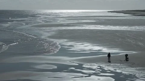 Two figures walk across reflective, icy beach Stock Footage 346258753