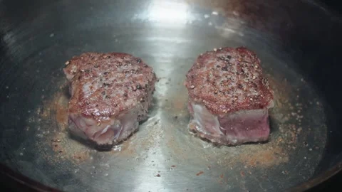 Two filet mignon steaks searing in a metal skillet Stock Footage 297123836