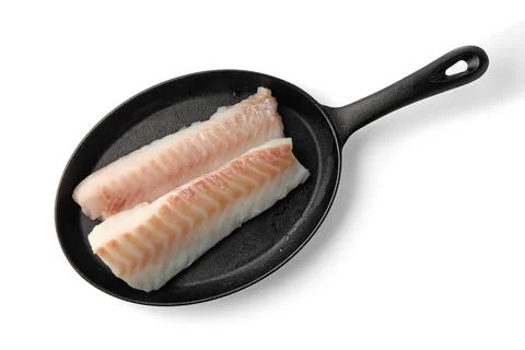 Two fillets of sea fish cod on a black cast iron frying pan isolated on whi.. Stock Photos