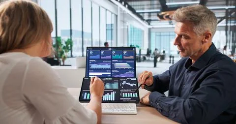 Two Finance Analysts Reviewing Data On Laptop, Discussing Market Trends. Stock Photos