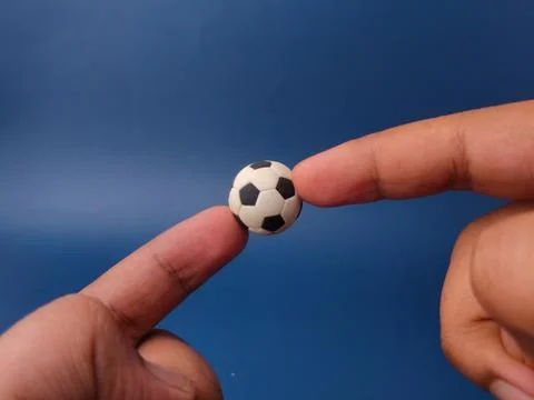 Two fingers balance a tiny black and white miniature toy soccer ball agains.. Stock Photos