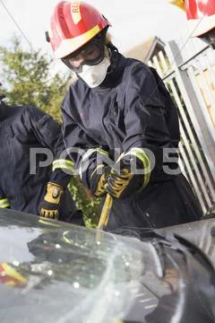 Two firefighters cutting out a windshield after an accident Stock Photos