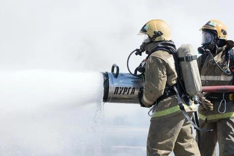 Two firefighters extinguish fire from fire hose, using firefighting water-foam Foto stock