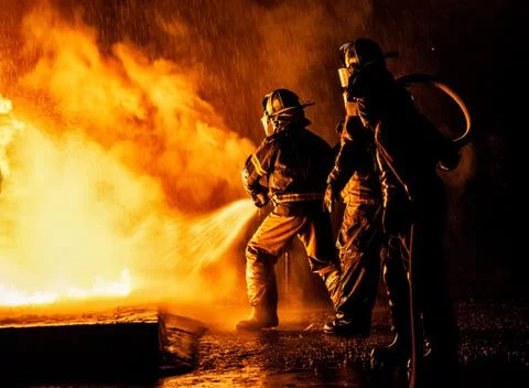 Two firefighters fighting a fire with a hose and water Stock Photos