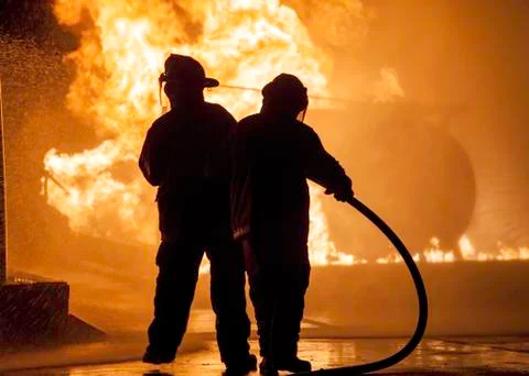 Two firefighters standing in front of a fire Stock Photos