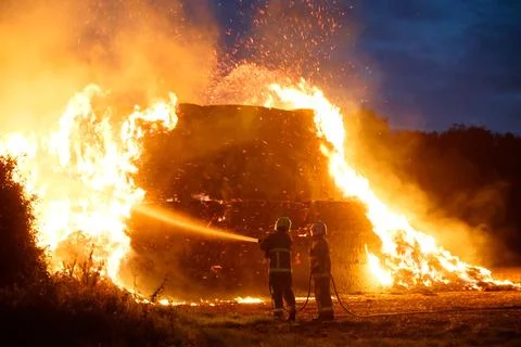 Two firemen putting out a fire on a haystack. UK Stock Photos