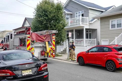 Two firemen stand on a sidewalk in front of an old house on a small street ne Stock Photos