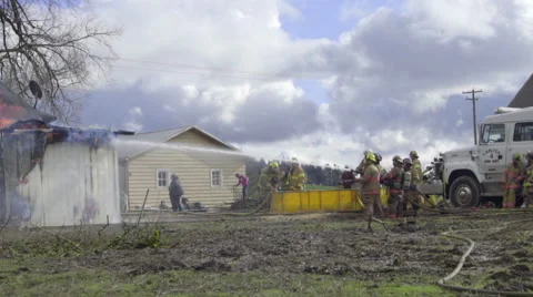 Two firemen teams water a burning home Stock Footage 61179797