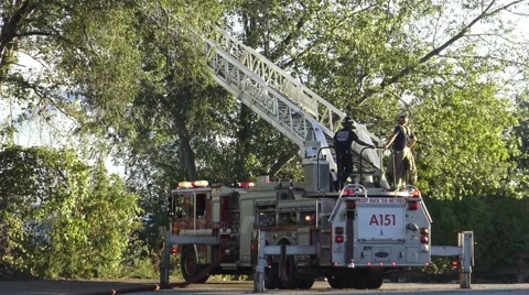 Two firemen on top of a fire truck with fire hose attached to a ladder platform Stock Footage