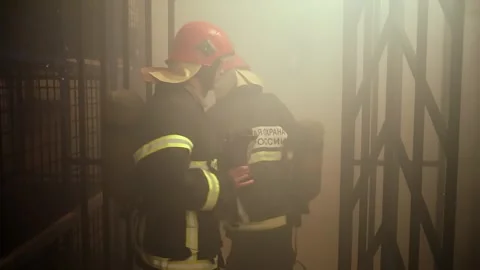 Two firemen walk out with gas masks from training room among smoke, russian 스톡 동영상 276368581