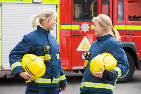 Two firewomen standing by fire engine talking Stock Photos