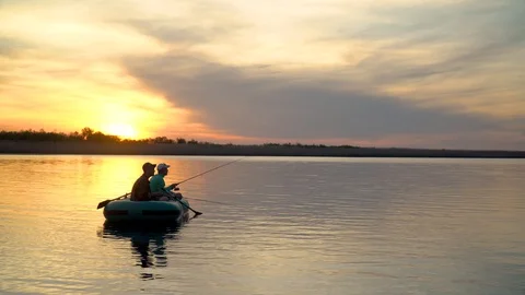 Two fishermen in the rays of the sunset catch fish from an inflatable boat 库存影片 128133592