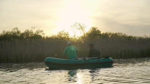 Two fishermen in the rays of the sunset catch fish from an inflatable boat 库存影片 128133641