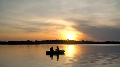 Two fishermen in the rays of the sunset catch fish from an inflatable boat 库存影片 128134056