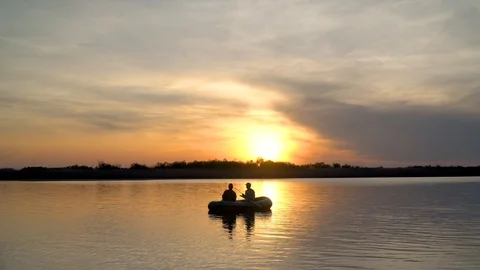 Two fishermen in the rays of the sunset catch fish from an inflatable boat 库存影片 128135318