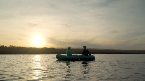 Two fishermen in the rays of the sunset catch fish from an inflatable boat Stock Footage 128135882