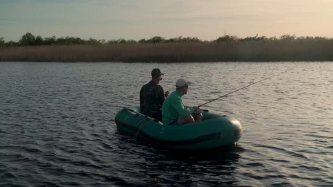 Two fishermen in the rays of the sunset catch fish from an inflatable boat 库存影片 128135987