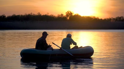 Two fishermen in the rays of the sunset catch fish from an inflatable boat 库存影片 128136987