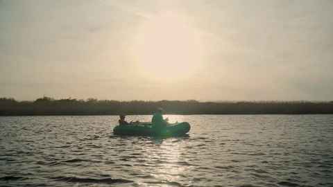 Two fishermen in the rays of the sunset catch fish from an inflatable boat 库存影片 128137061