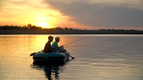 Two fishermen in the rays of the sunset catch fish from an inflatable boat 库存影片 128137811