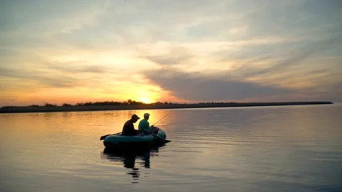 Two fishermen in the rays of the sunset catch fish from an inflatable boat Stock Footage 128138574