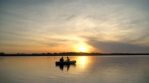 Two fishermen in the rays of the sunset catch fish from an inflatable boat Stock Footage 128138677
