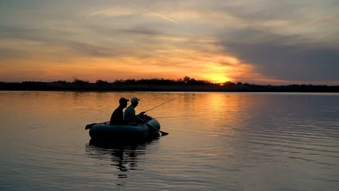 Two fishermen in the rays of the sunset catch fish from an inflatable boat Stock Footage 128138725