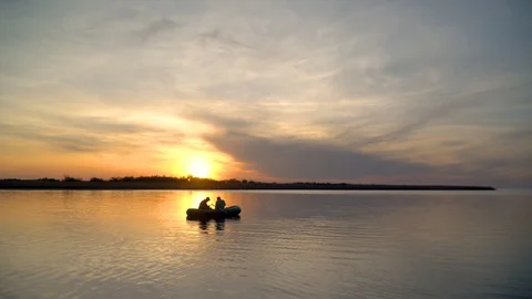 Two fishermen in the rays of the sunset catch fish from an inflatable boat Stock Footage 128139029