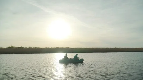 Two fishermen in the rays of the sunset catch fish from an inflatable boat Stock Footage 128139108