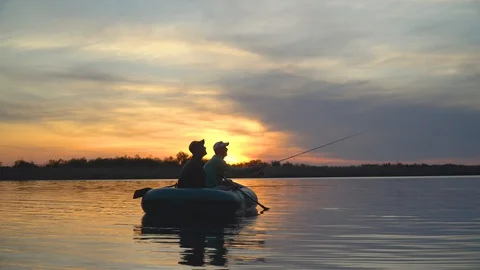 Two fishermen in the rays of the sunset catch fish from an inflatable boat Stock Footage 128139147