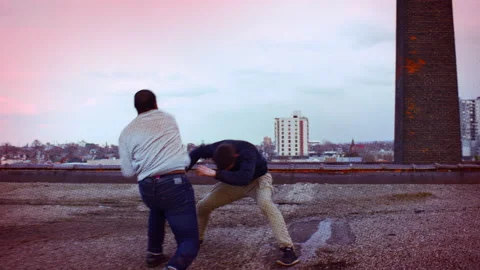 Two fit men fight each other on top of a roof and one man punches the other in t Stock Footage 199456156