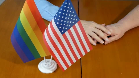 Two flags united state of america and lgbt and woman hands on wooden table Video stock 163573398
