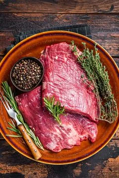 Two Flap or Flank raw beef steaks on a rustic plate with herbs. Dark wooden Stock-Fotos
