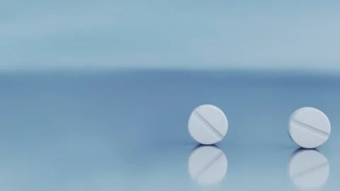 Two flat, round medical tablets are rolling across a glass table surface Stock Footage 293795539