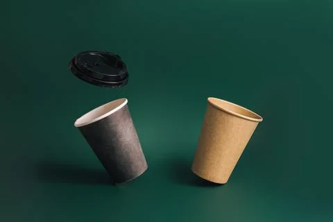 Two floating disposable cups and lid against green background Stock Photos