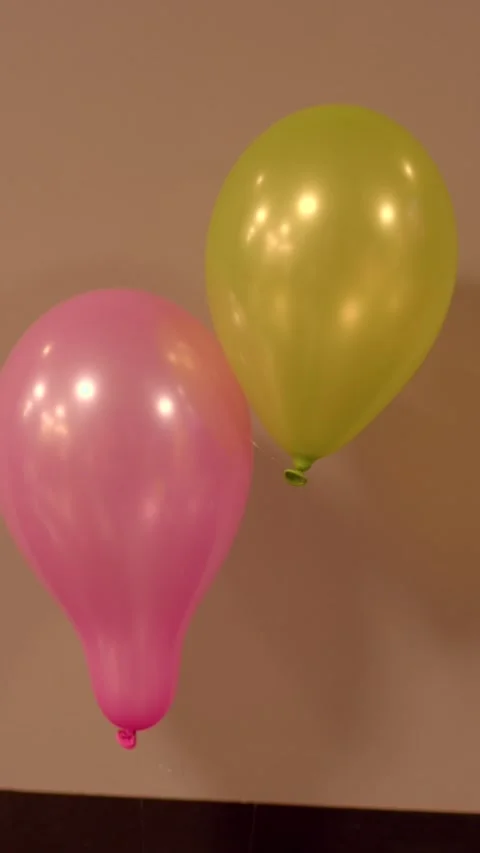 Two floating latex balloons against a beige wall with soft studio light Stock Footage 336533927