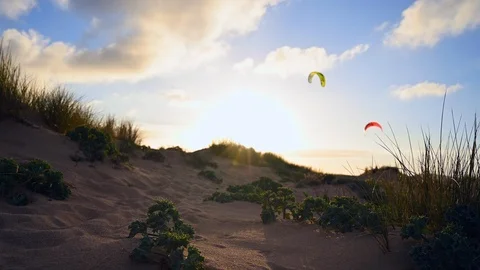 Two flying kitesurfs,clouds running fast, sand dunes at sunset Stock Footage 107105738