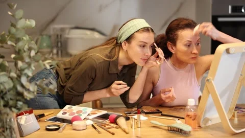 Two focused female friends carefully applying makeup while looking into vanity Stock Footage 318944934