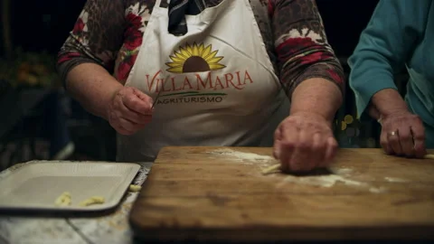 Two focused Italian cooks rolling out dough and forming spiral pasta shapes for Stock Footage 199456788