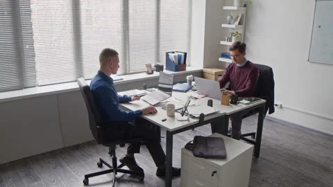 Two Focused Office Workers Passing Folder while Using Laptops at Desk in Office Stock Footage 313554024
