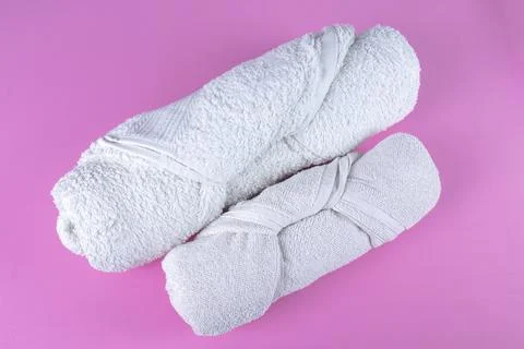 Two folded rolled white bathroom towels on pink background. Stock Photos