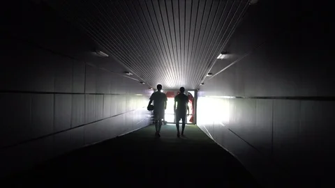Two football players are walking along a dark tunnel to the football field. View Stock Footage