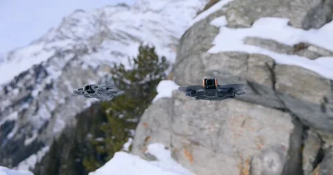Two FPV drones hover and fly side by side near snowy alpine rocks, testing Stock Footage 343928017