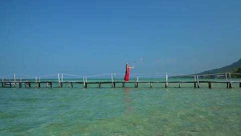 Two frames in video. Beautiful woman walking down pier in long red dress. Phu Stock Footage 87528434