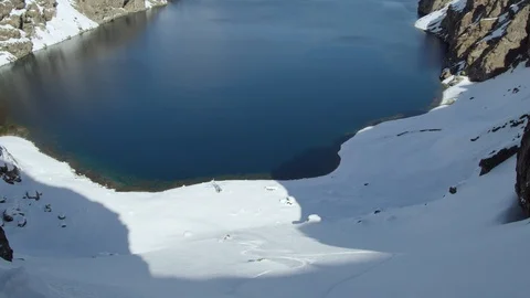 Two freeride snowboarders riding down rocky terrain, stopping by lake shore Stock Footage 121597100