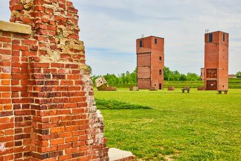 Two freight elevator towers with busted brick pillars and benches in green field 스톡 사진