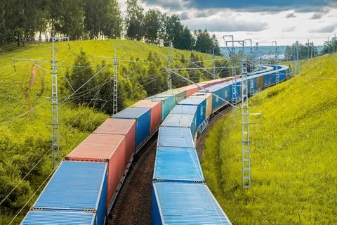 Two freight trains move in parallel, carrying colorful containers along railway Stock Photos
